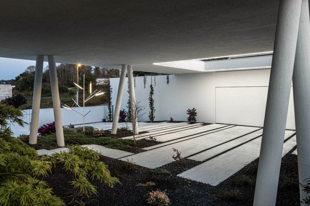 A silent block of white striped concrete is the house that integrates with its surroundings through its serenity